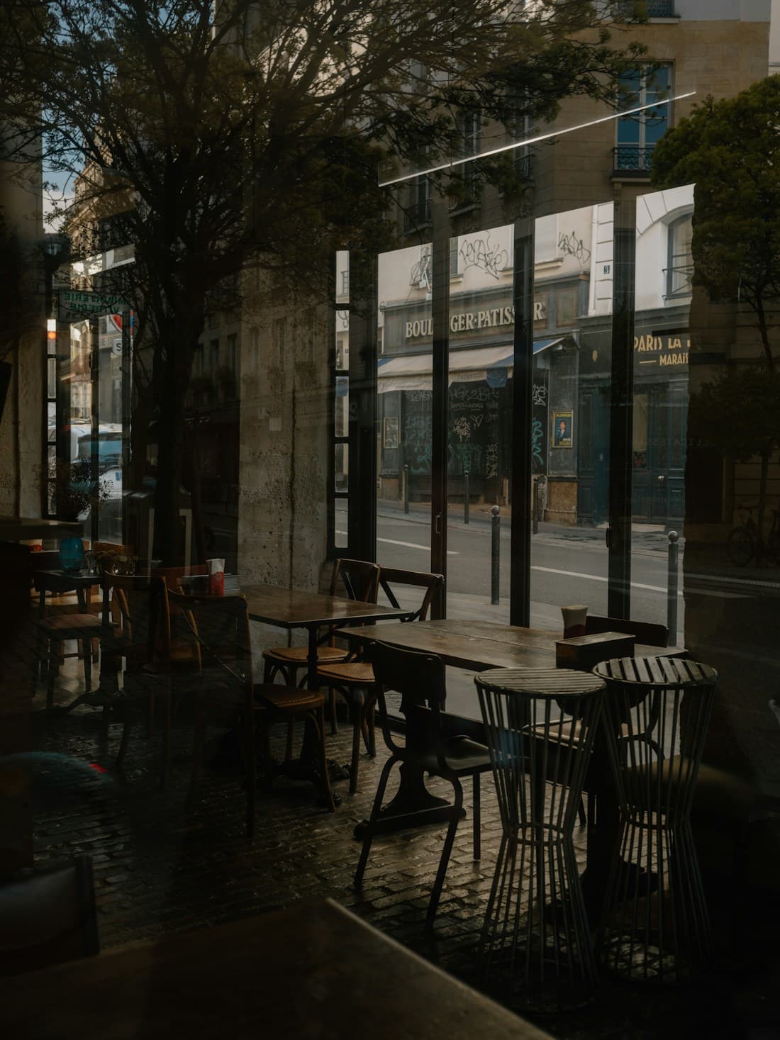 Tables et chaises d’un café parisien derrière sa vitrine